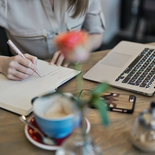 person writing on a notebook beside macbook